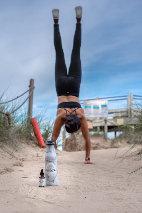 A woman with her hands on the ground and legs in the air next to a Blooming Botanicals CBD tincture