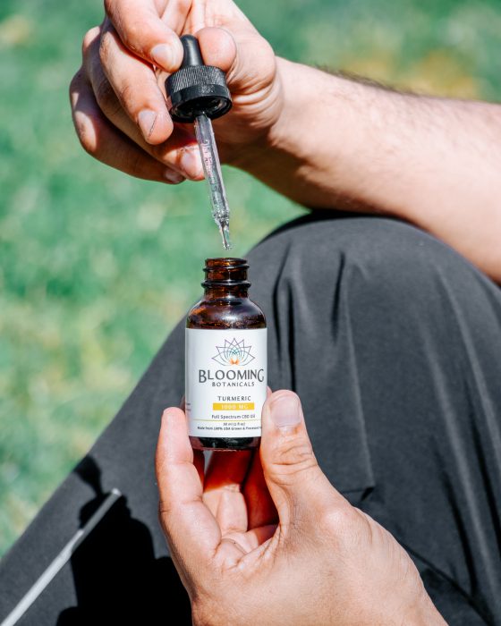 Two hands holding an open dropper bottle of tincture - dropper in one hand, bottle in the other.