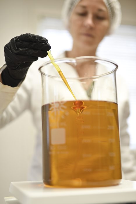 Woman formulating CBG in a lab with a lab coat and gloves. 